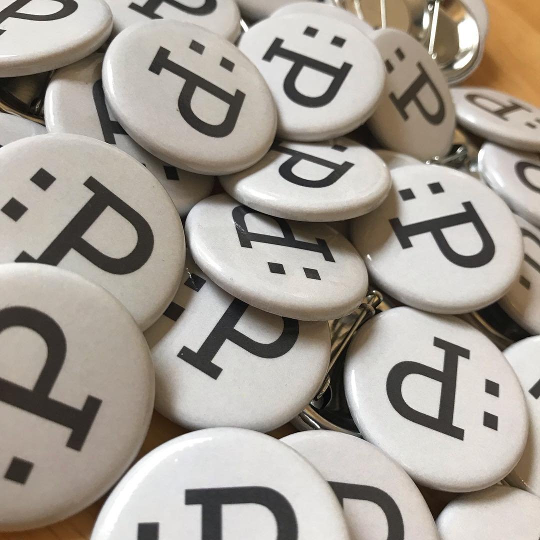 A pile of white pinback buttons printed with the Pixel Humor :P mark